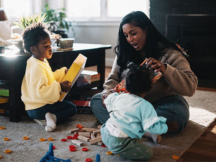 A parent playing with 2 young children on a living room floor