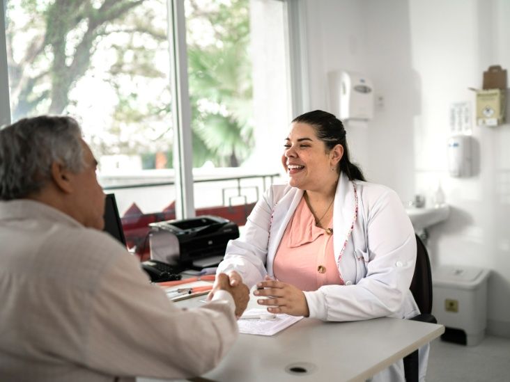 A smiling doctor shaking hands with a patient across a desk