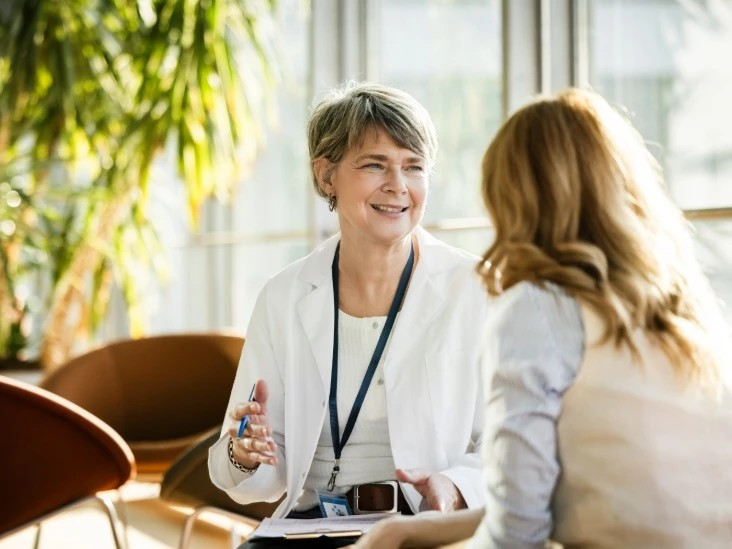 A clinician in a white coat talking with a person in a sunlit office