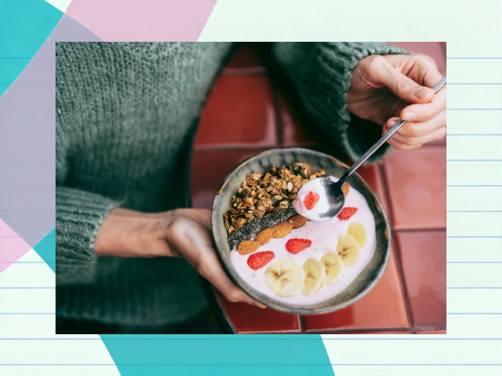Hands holding a bowl of yogurt topped with granola, chia seeds, almonds, strawberries, and banana