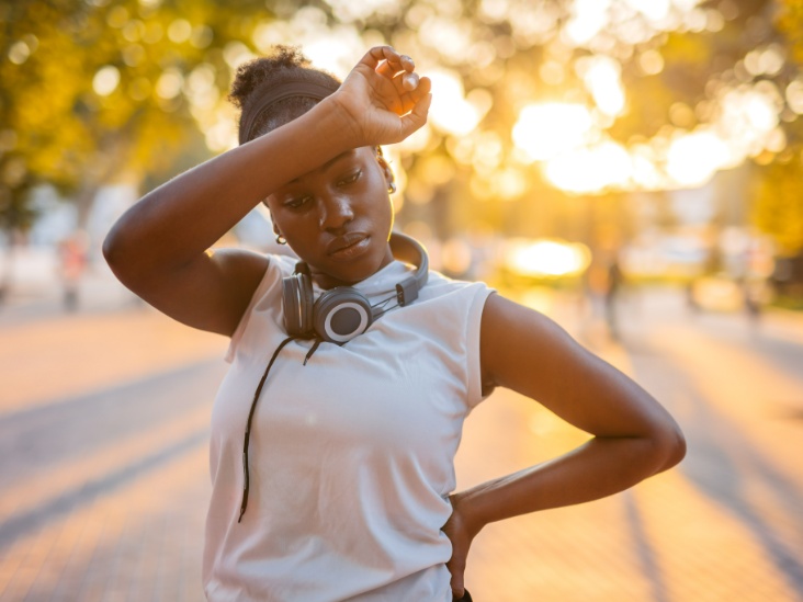 A person outdoors at sunset resting a hand on their forehead